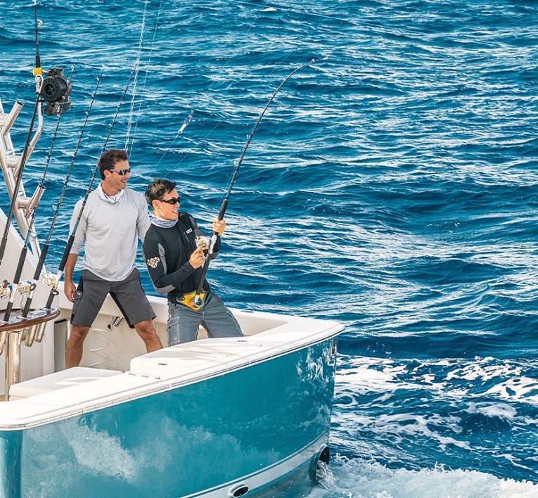 Two men fishing on the back of a boat reeling in a fish 