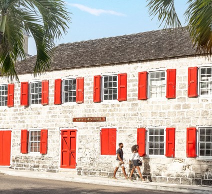 a couple of people walking by a building with red shutters