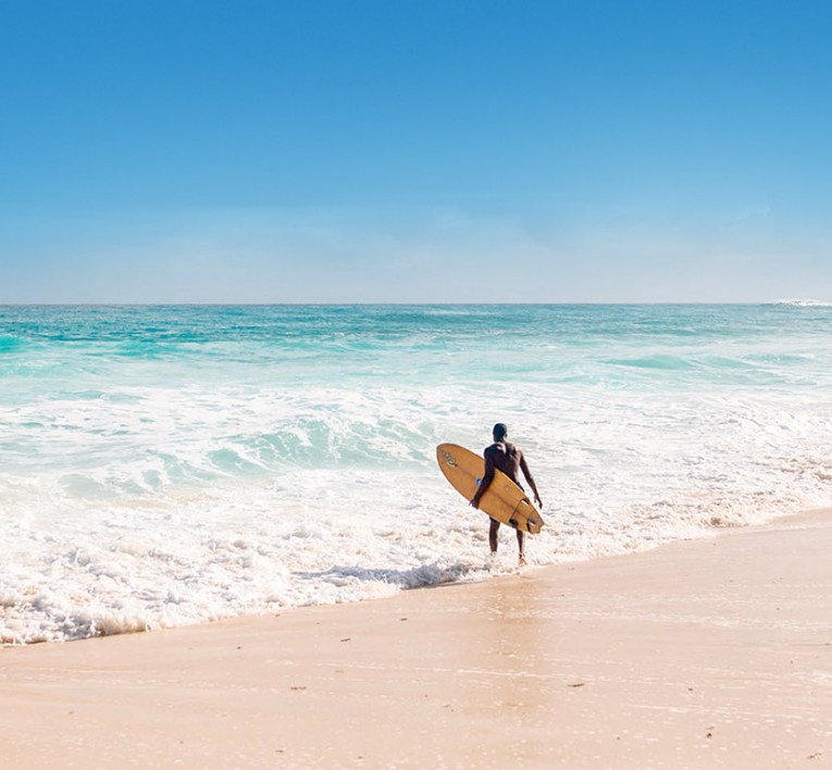 man holding surfboard while walking into the ocean